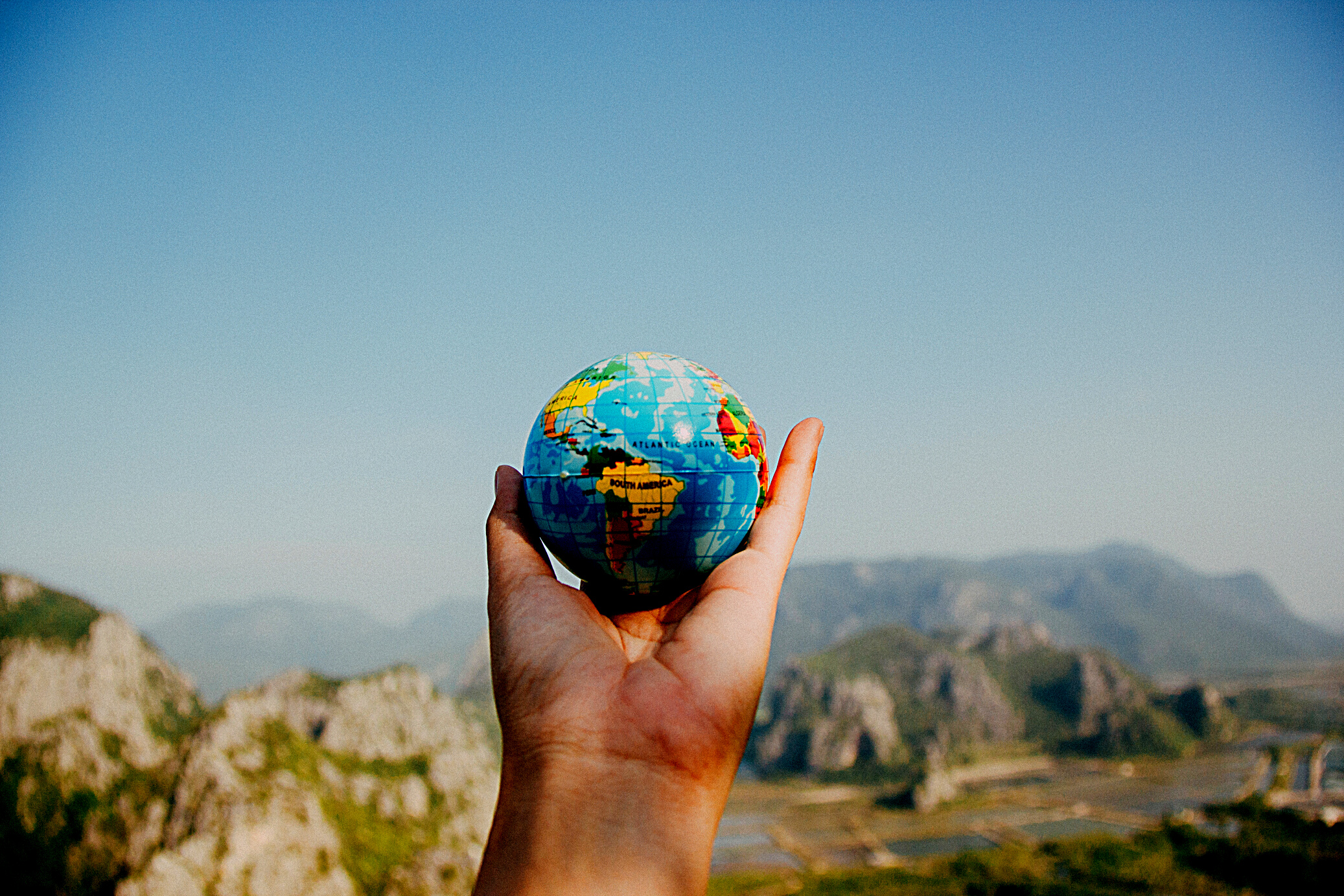 Person Holding World Globe Facing Mountain