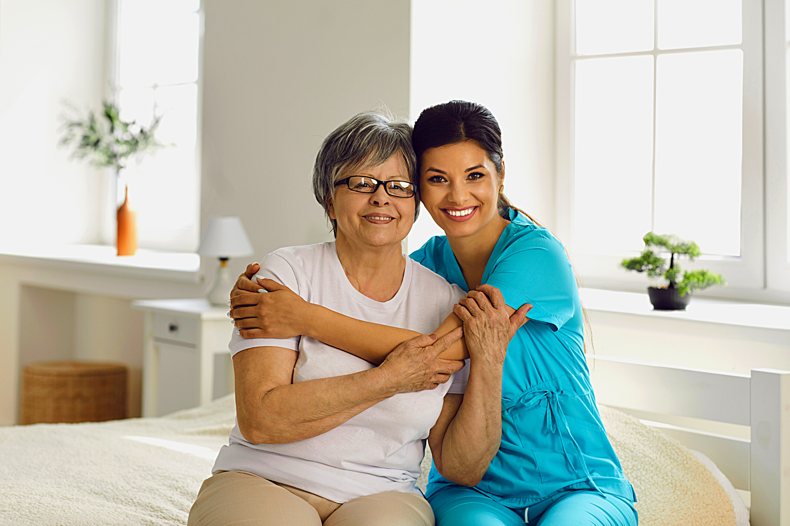Portrait of Happy Caregiver Together with Senior Patient Sitting on Bed in Retirement Home