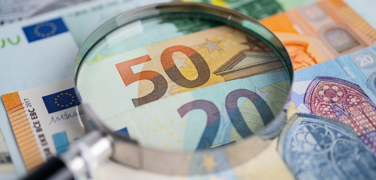 Image of a stack of currency and a magnifying glass